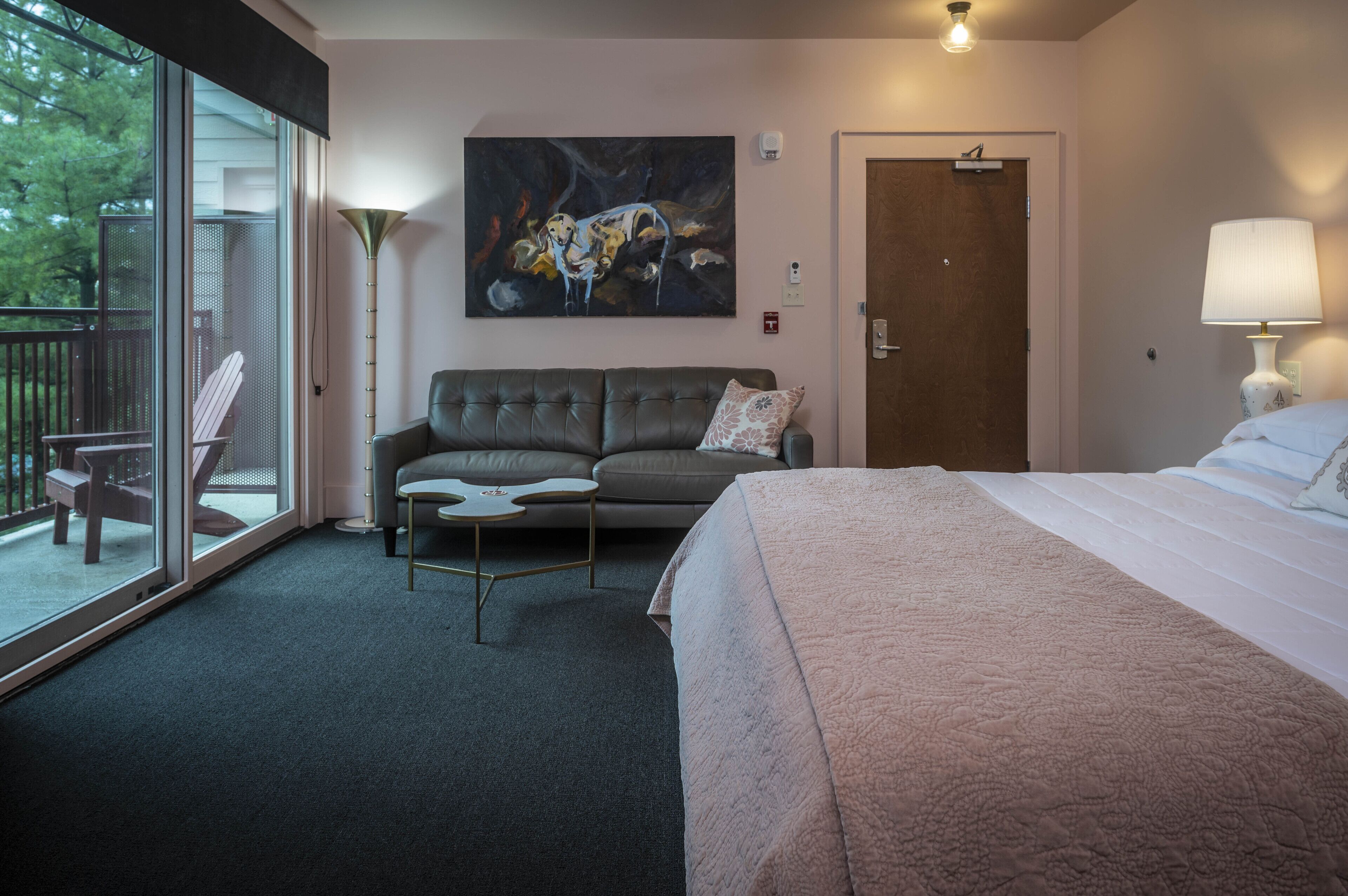 A hotel room with a large bed, a sofa, a coffee table, and a painting on the wall.