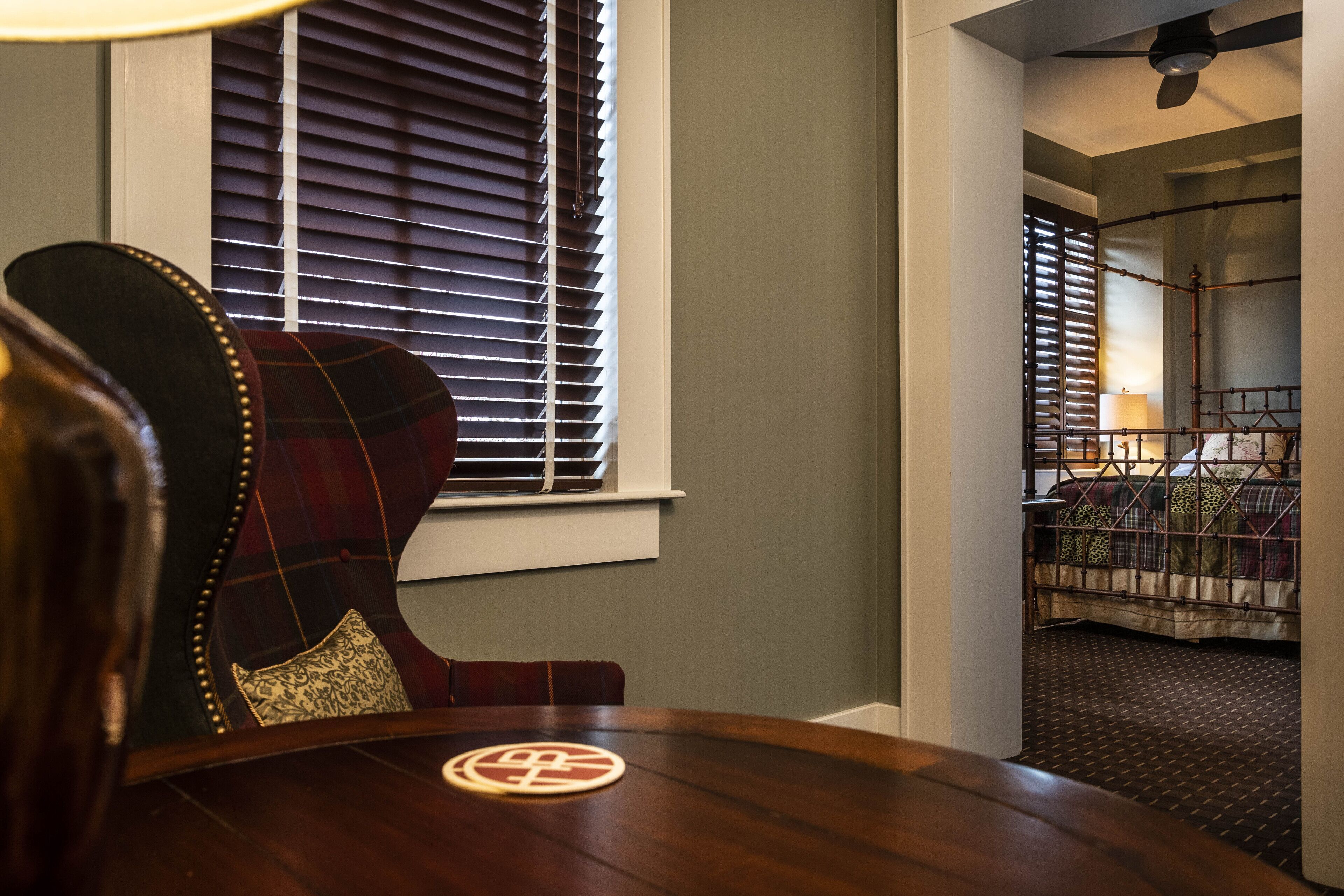 A dining area with a wooden table, a plaid chair, and a window with blinds.