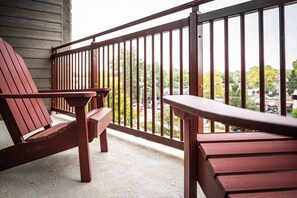 A wooden deck with a metal railing, two wooden chairs, and a bench.