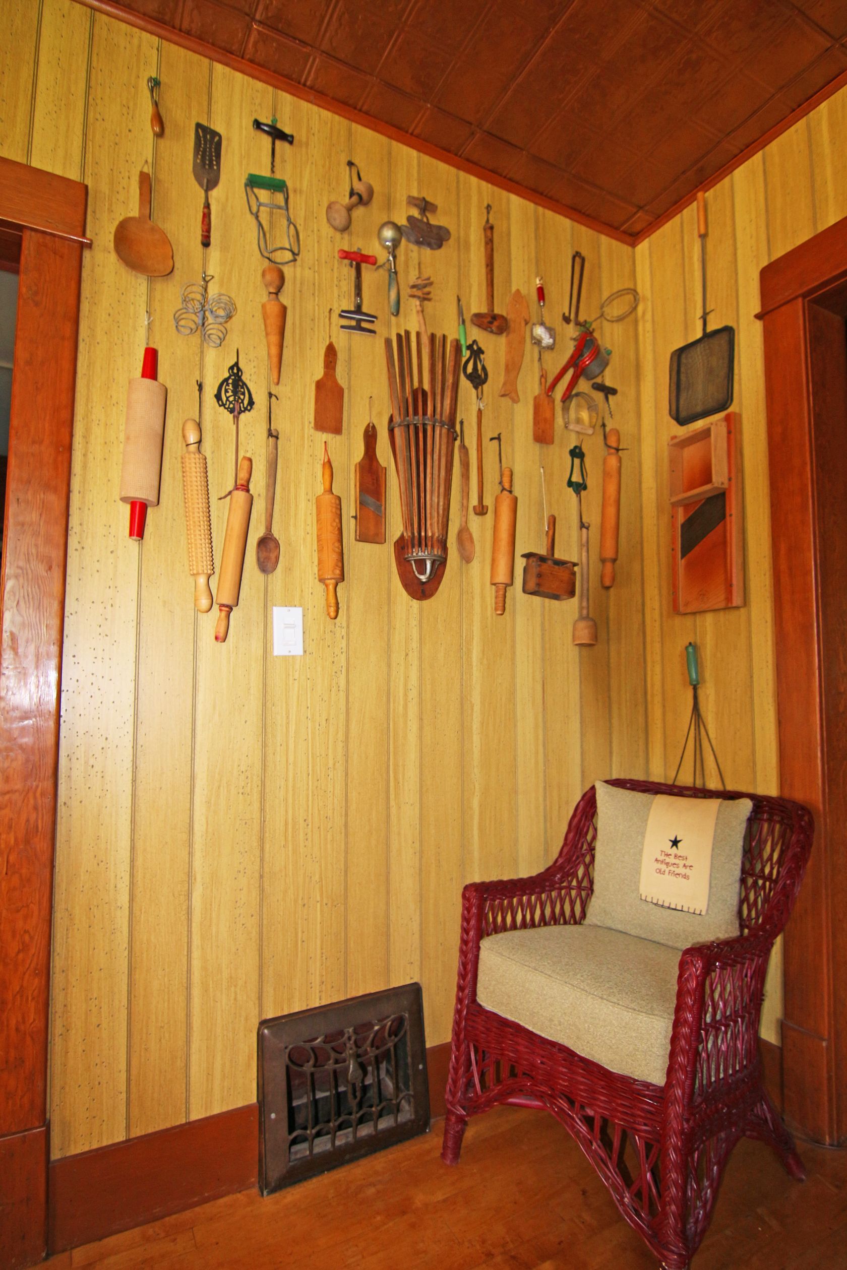 A room with wooden paneling, a wicker chair, and various kitchen utensils hanging on the wall.