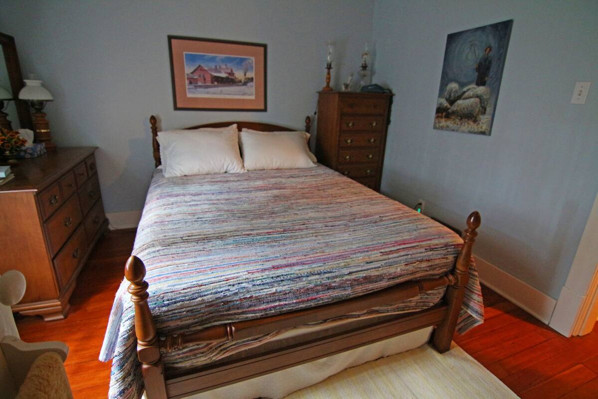 Ein Schlafzimmer mit einem hölzernen Bett, einem Schminktisch, einem Sessel und zwei gerahmten Bildern an der Wand.