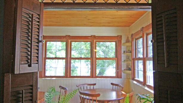Un comedor con mesa y sillas de madera, un ventanal con vidrieras y vistas a la vegetación exterior.