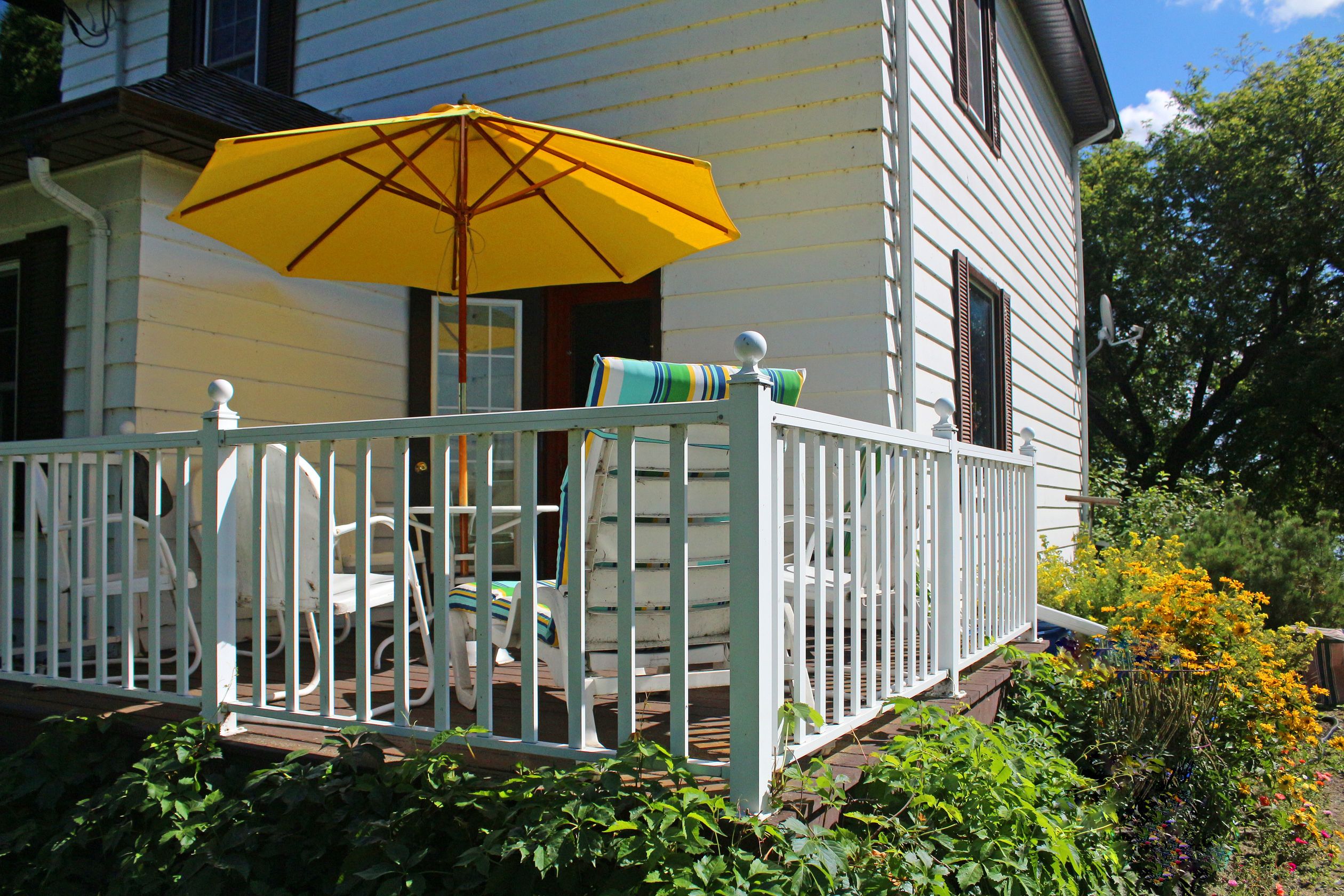 A white house with a porch, a yellow umbrella, and a white railing.
