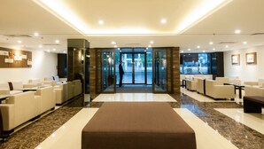 Una hall d'albergo con un'area salotto centrale, una reception e un ingresso in vetro.