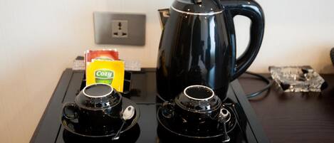 A coffee station with a black coffee pot, two black cups, and a box of 'Cozy' tea.