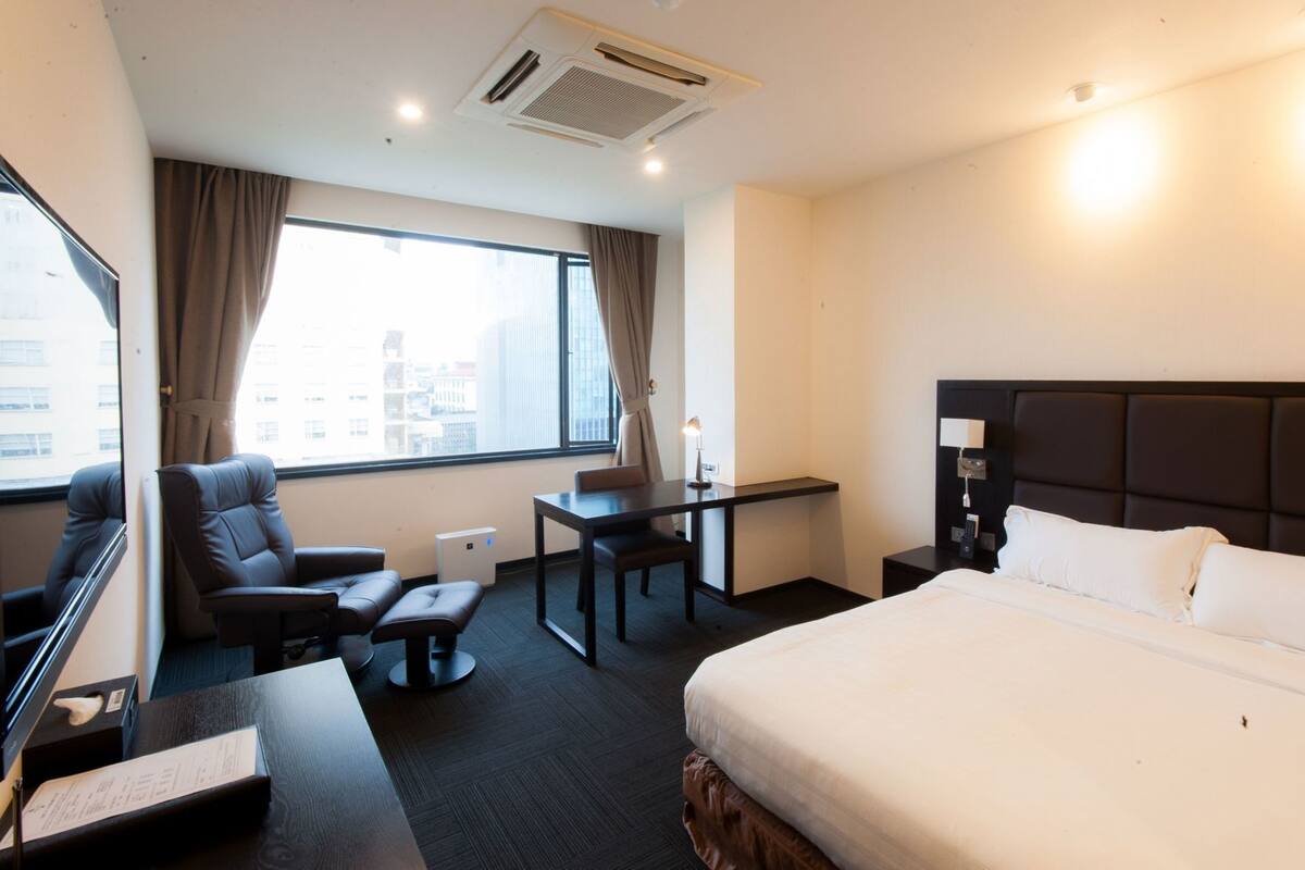 Ein Hotelzimmer mit Bett, Schreibtisch, Stuhl und Blick auf die Stadt.