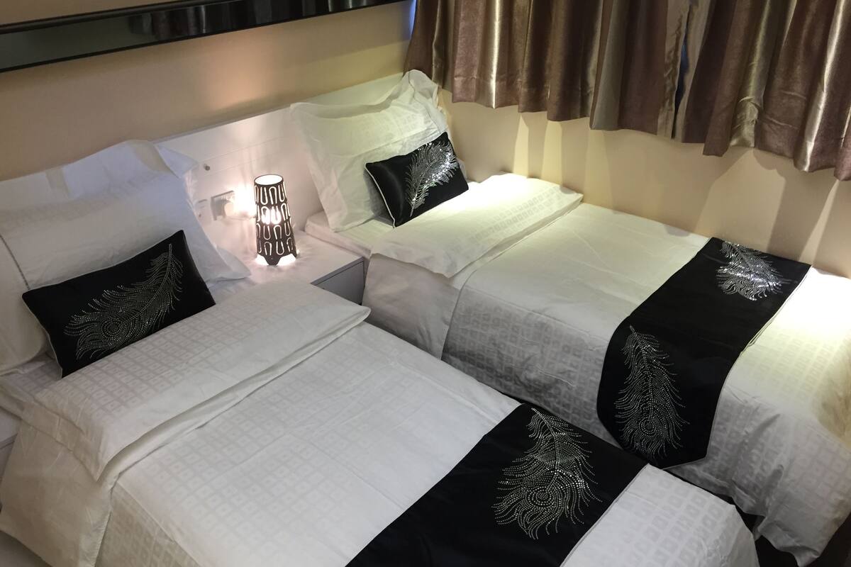 Ein Hotelzimmer mit zwei Betten, jeweils mit weißer Bettwäsche und schwarzen Zierkissen. Zwischen den Betten befindet sich ein Nachttisch mit einer Lampe.