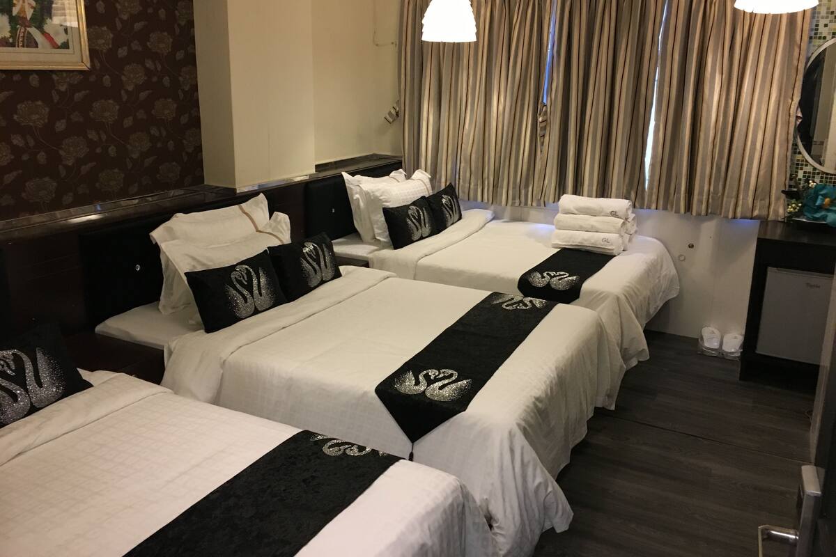 Ein Hotelzimmer mit zwei Betten, jeweils mit weißer Bettwäsche und schwarzen Kopfteilen, einem Schreibtisch mit Spiegel sowie einem Duschbereich.