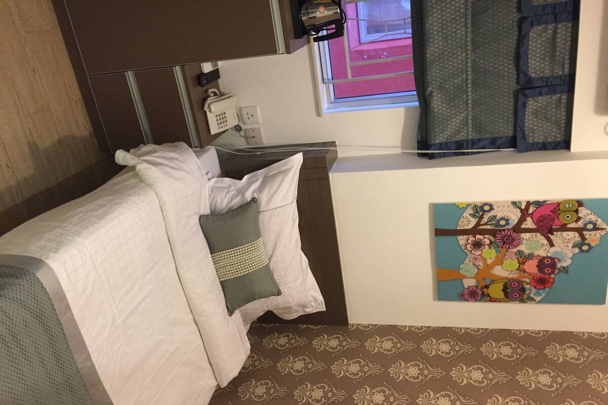 Ein Hotelzimmer mit Bett, Fenster mit Blick, einem wandmontierten Telefon und einem dekorativen Kunstwerk.