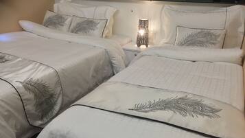 Habitación de hotel con dos camas, cada una con una cubierta de edredón estampada con motivos florales y almohadas a juego. Se observa una mesita de noche con lámpara entre las camas.