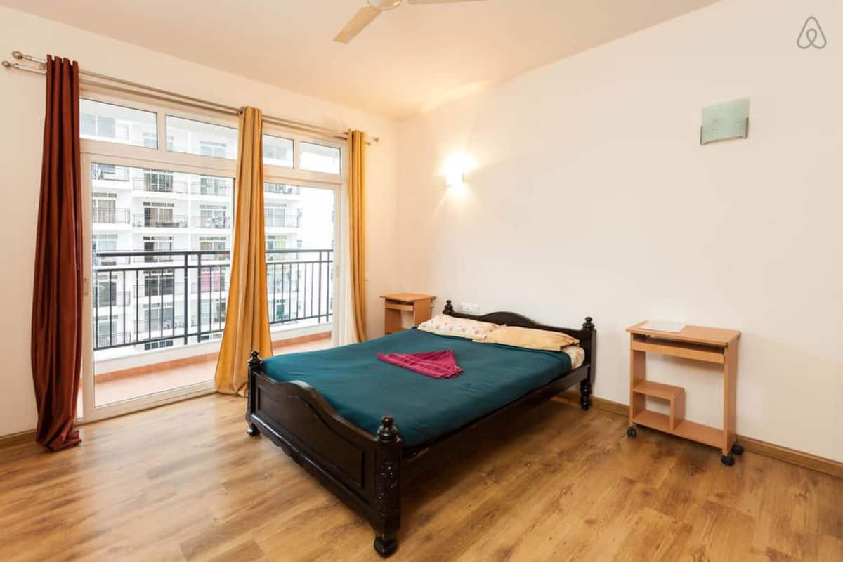 A bedroom with a large window, a bed, a bedside table, and a nightstand.
