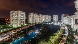 Un edifici residencial de grans alçades de nit, amb finestres il·luminades, una piscina central i vegetació als voltants.