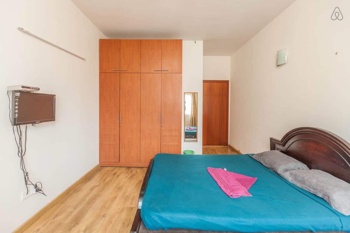 A bedroom with a bed, wooden wardrobe, and a television on the wall.