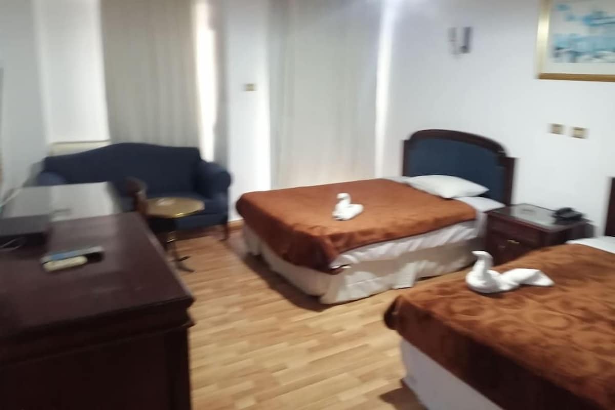 Una habitación de hotel con cama, una silla, un escritorio y una mesita de noche.
