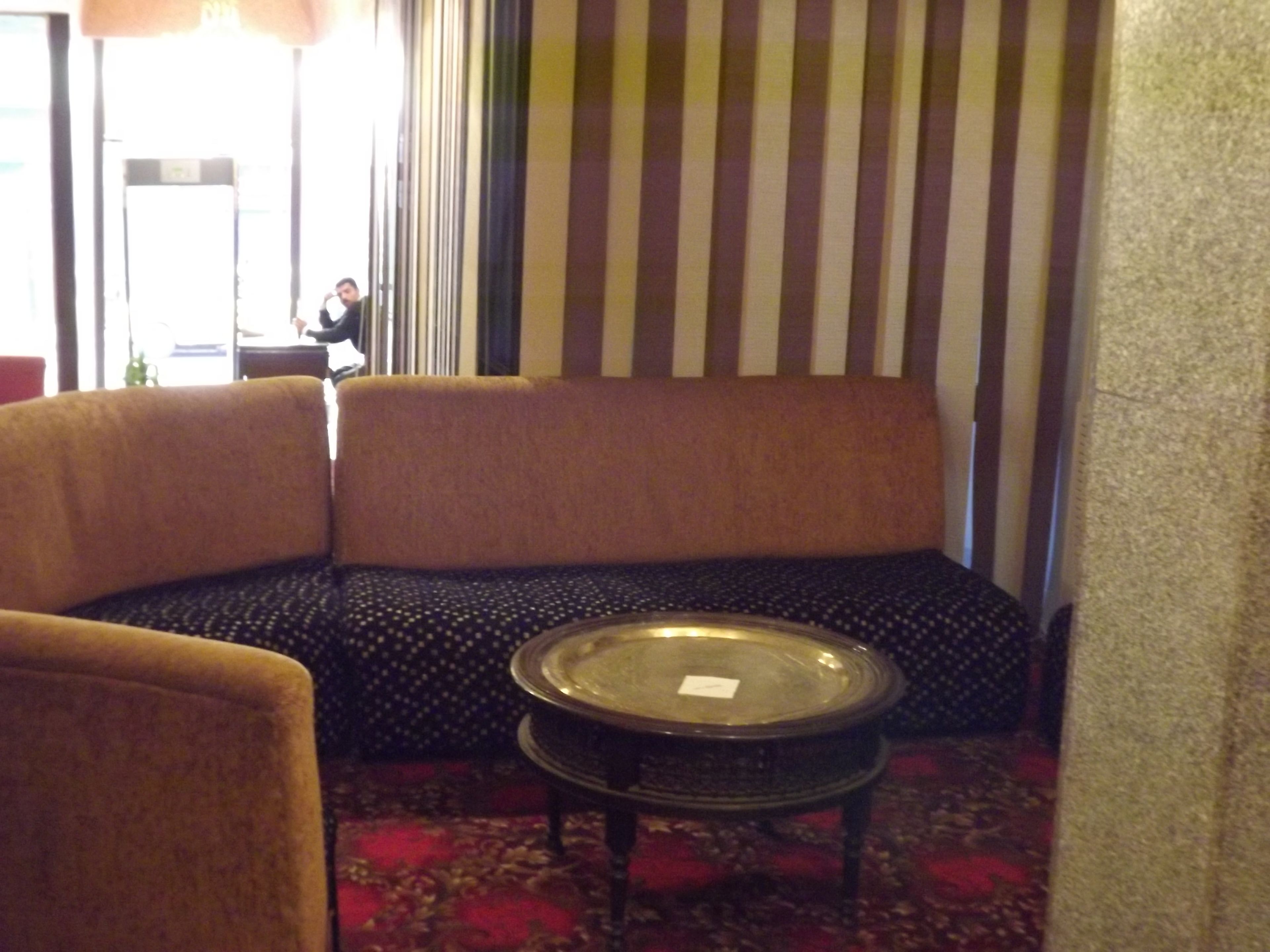 Een zithoek met een bank en fauteuils, een klein rond tafeltje en een kamerbreed tapijt met een patroon.