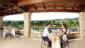 Ein überdachter Außenbereich zum Essen mit Steinsäulen, Tischen und Stühlen, mit Blick auf eine reizvolle Landschaft.