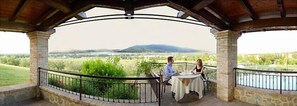 A covered outdoor seating area with stone pillars and a view of a vineyard and distant hills. - Tenuta del Perugino (Bettona)