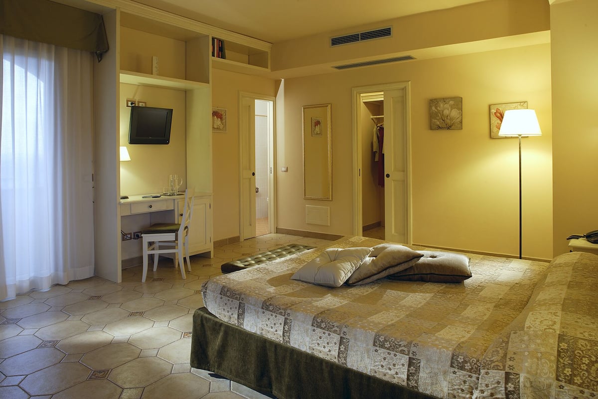Una habitación de hotel con cama, escritorio, silla, televisor y lámpara.
