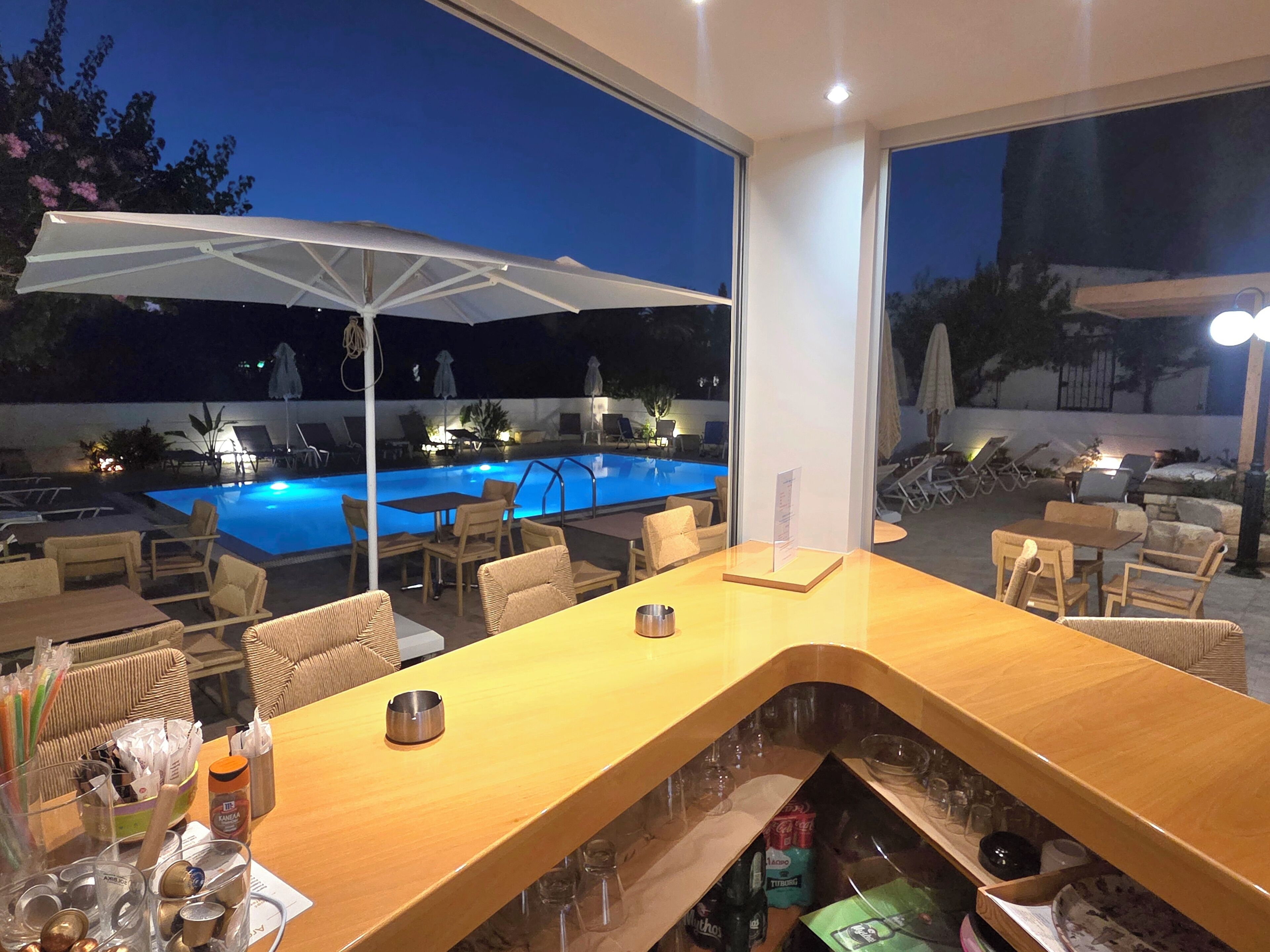 Zona de bar con vista a la piscina, asientos exteriores y una sombrilla grande.