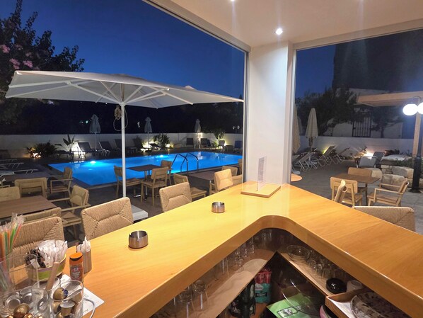 Zona de bar amb vista a la piscina, seients a l'aire lliure i un parasol gran.