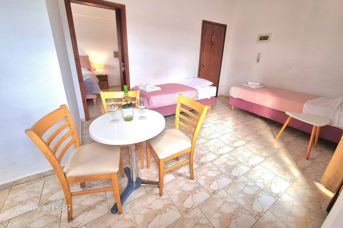 A small, well-lit room with a bed, a sofa, a table with chairs, and a bottle of wine.