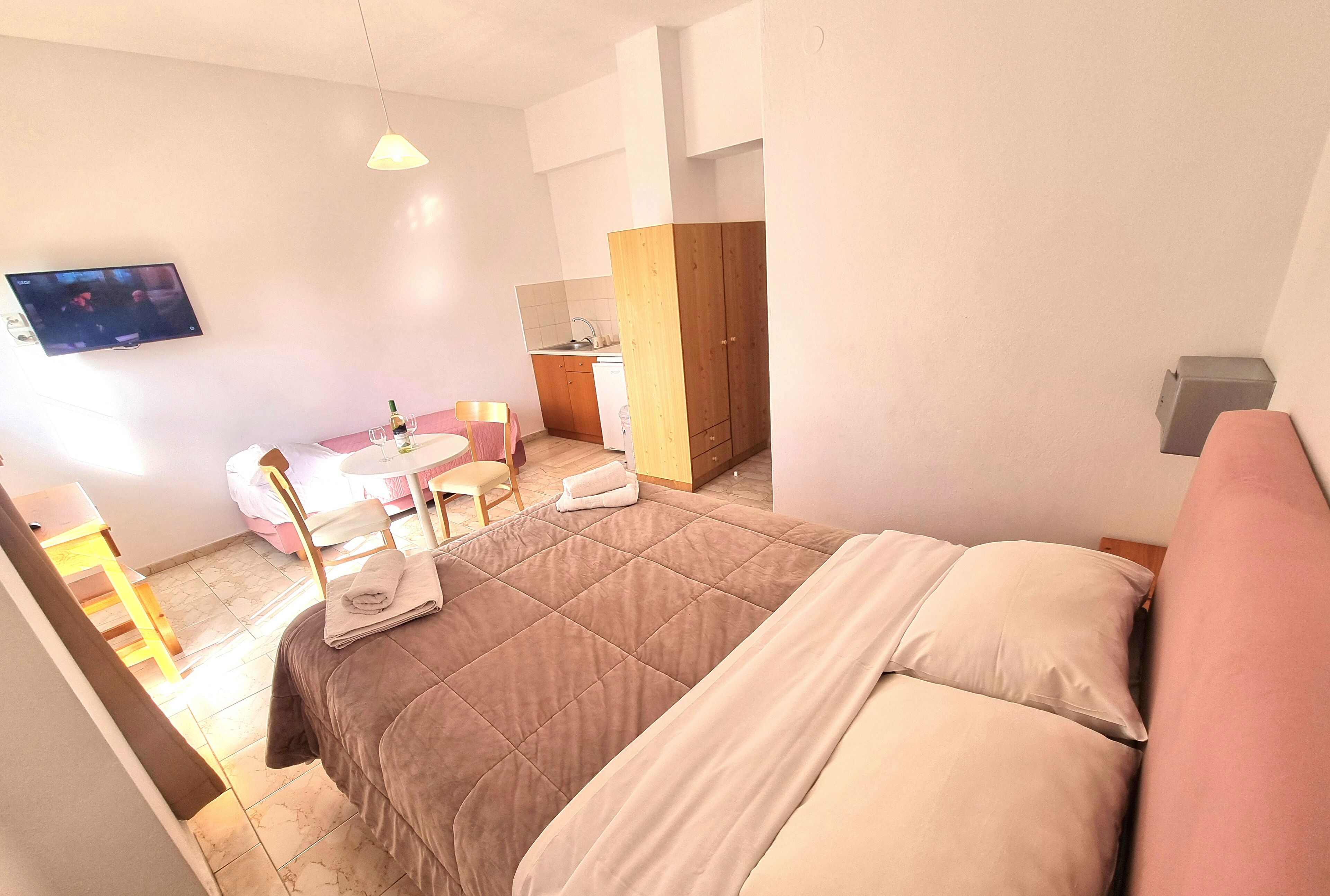 A hotel room with a bed, a small table with chairs, a TV, and a kitchenette.