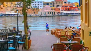 A riverside café with outdoor seating overlooking a river, surrounded by colorful buildings. - Archontiko (Malevizi)