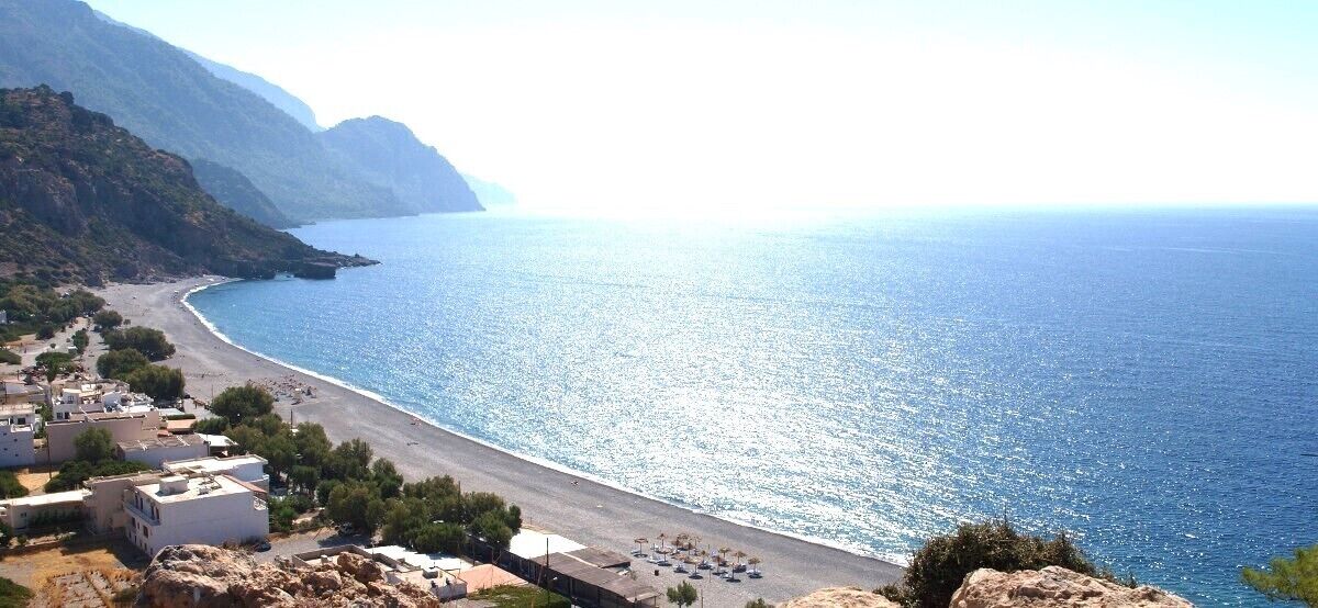 Un pueblo costero con una playa, edificios y montañas al fondo.