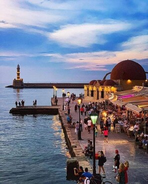 A waterfront promenade with a lighthouse, a domed building, and people walking along the path.