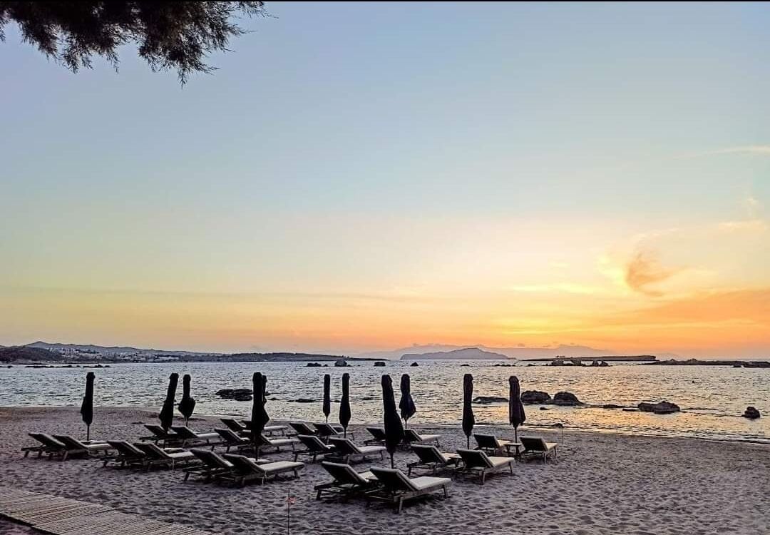 A beach with sun loungers and umbrellas, a calm sea, and a sunset.