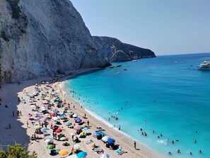 A beach with clear turquoise water, rocky cliffs, and numerous umbrellas.