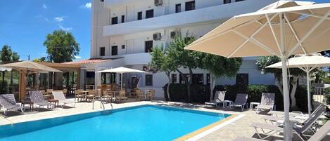 Una piscina al aire libre, sombrillas, sillones reclinables de piscina