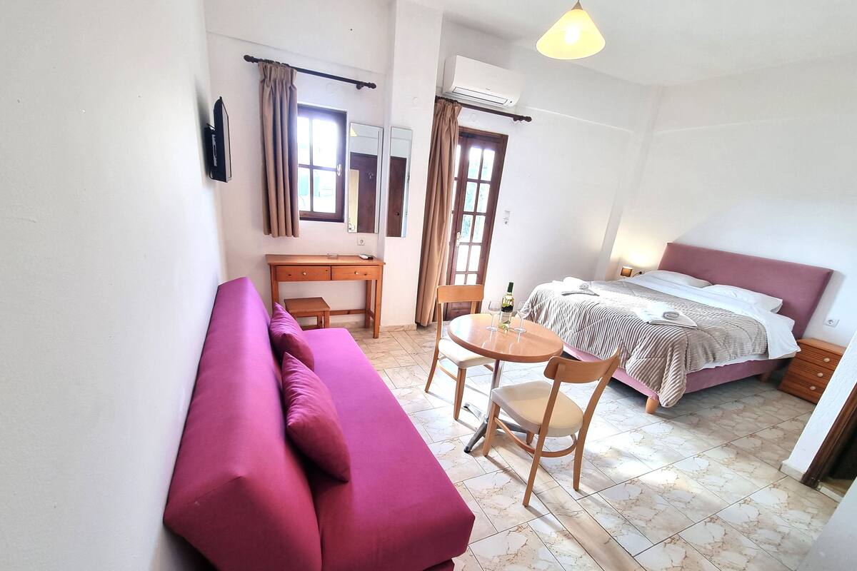A compact bedroom with a bed, a small table with chairs, a sofa, and a desk.