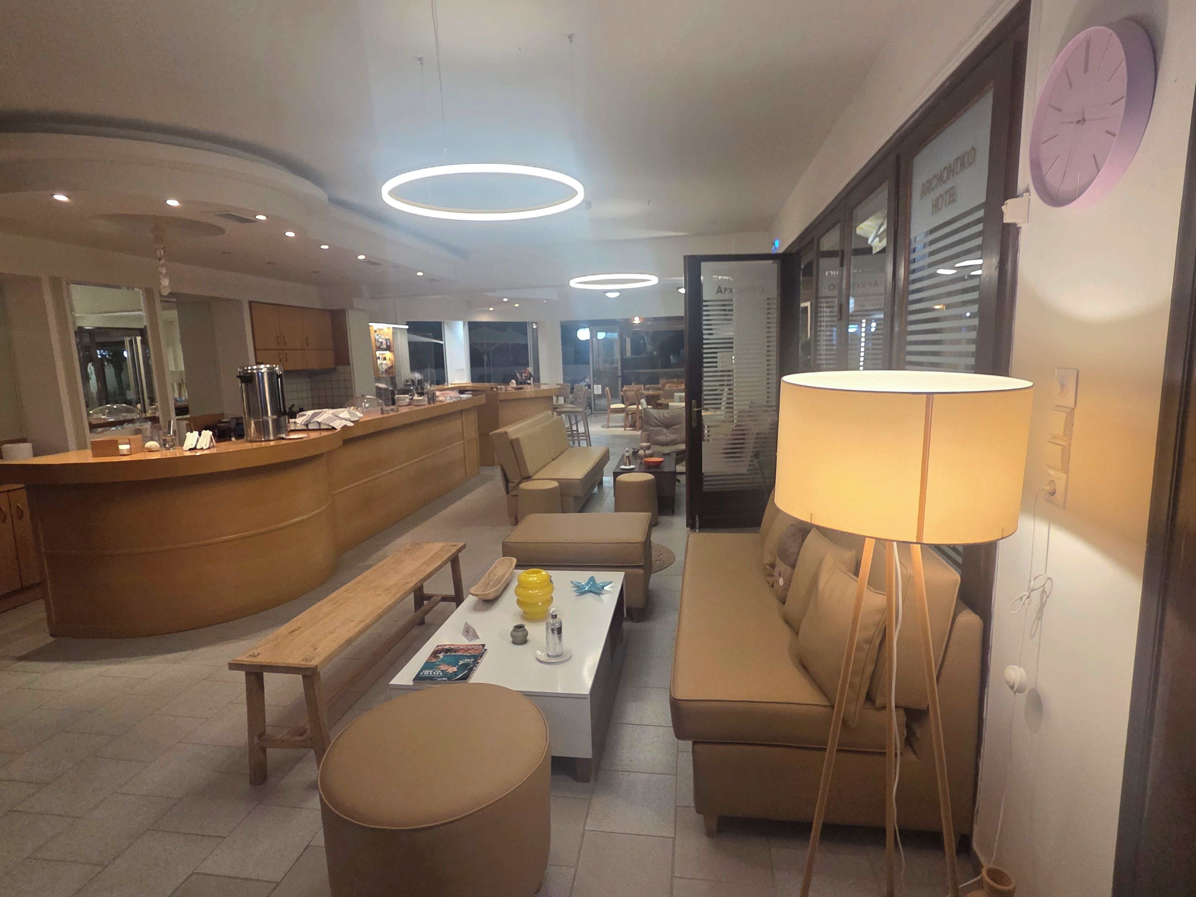 A modern hotel lobby with a reception desk, seating area, and a large wall clock.