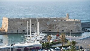 A historic stone fortress with a moat, surrounded by a marina with boats, palm trees, and a clear view of the sea. - Archontiko (Malevizi)