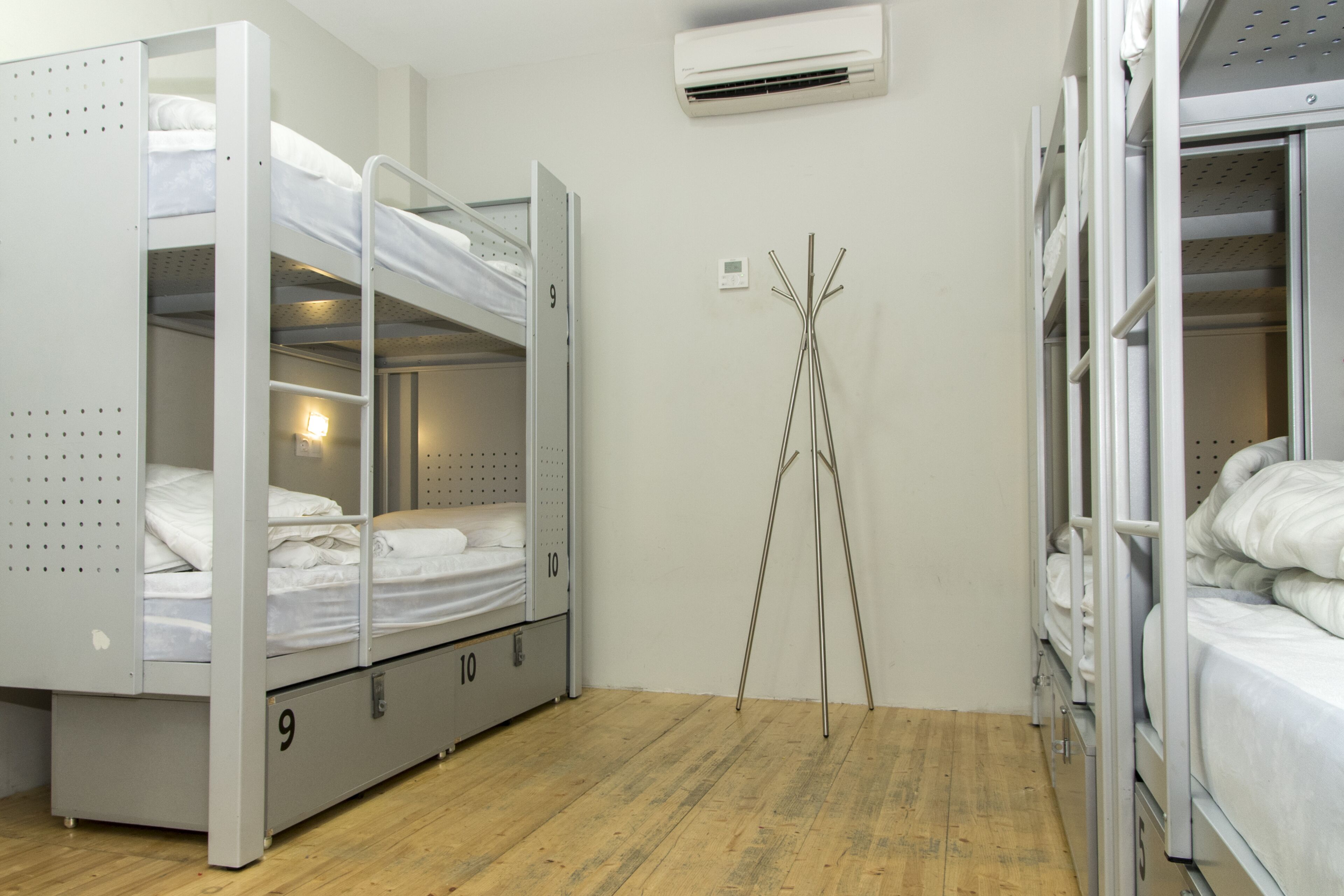 A dormitory room with bunk beds, a wooden floor, and an air conditioning unit on the wall.