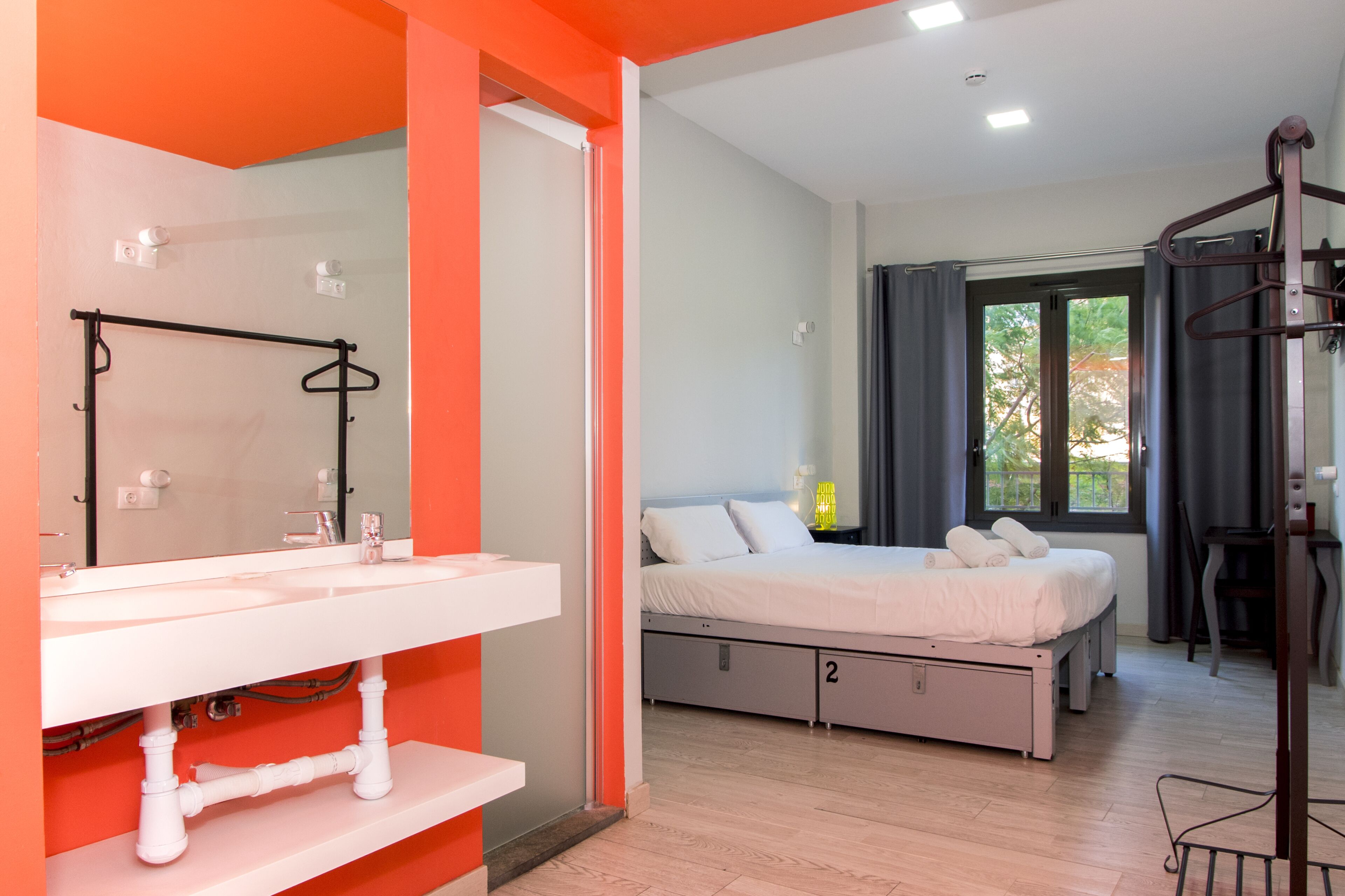 Ein modernes Schlafzimmer mit einem weißen Bett, ein Badezimmer mit einem weißen Waschbecken und ein Blick ins Freie durch ein Fenster.