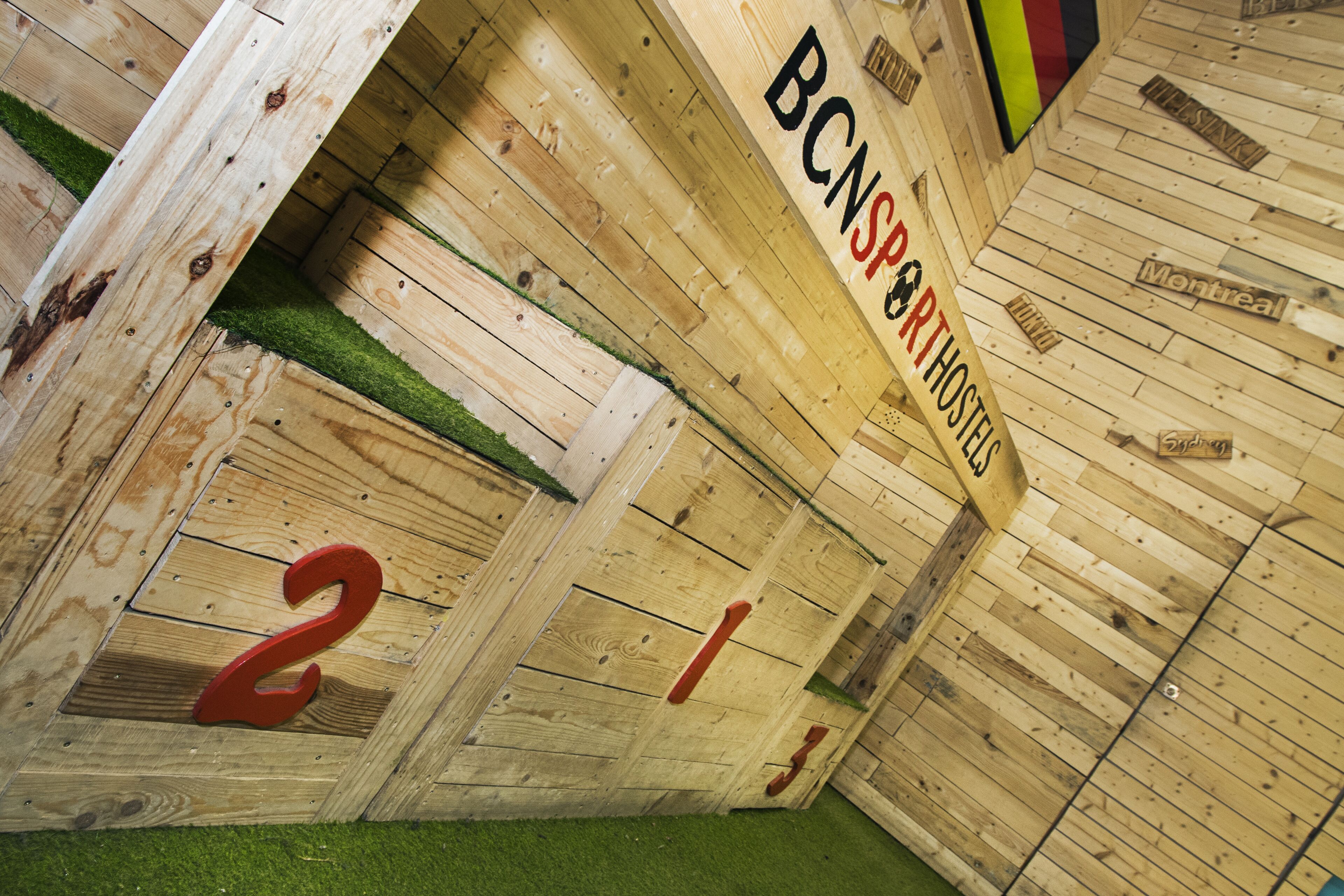 A wooden cabin with a rustic interior, featuring a wooden wall with the text "BCNSPORTHSTELLE" and a number "2" on the door.