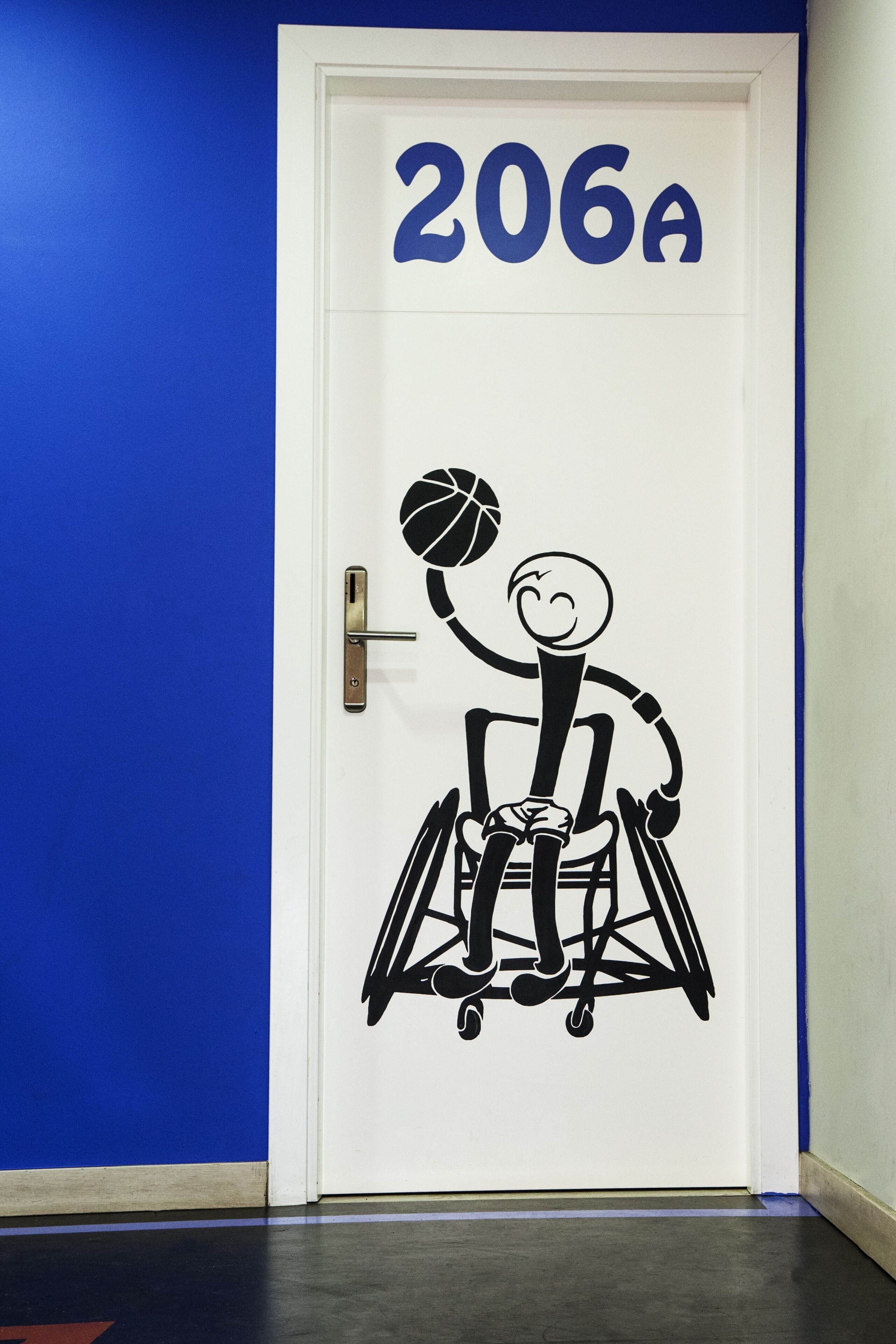 Una puerta con el número 206A y un dibujo de una persona en silla de ruedas jugando al baloncesto.