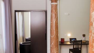 Habitación de hotel moderna con un escritorio de tonos oscuros, una pequeña estatua, una silla negra curvada, una columna de mármol grande y un espejo que refleja la habitación.