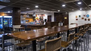 Un restaurant doté d’une longue table en bois, de chaises en osier et d’un bar proposant divers plats et boissons.