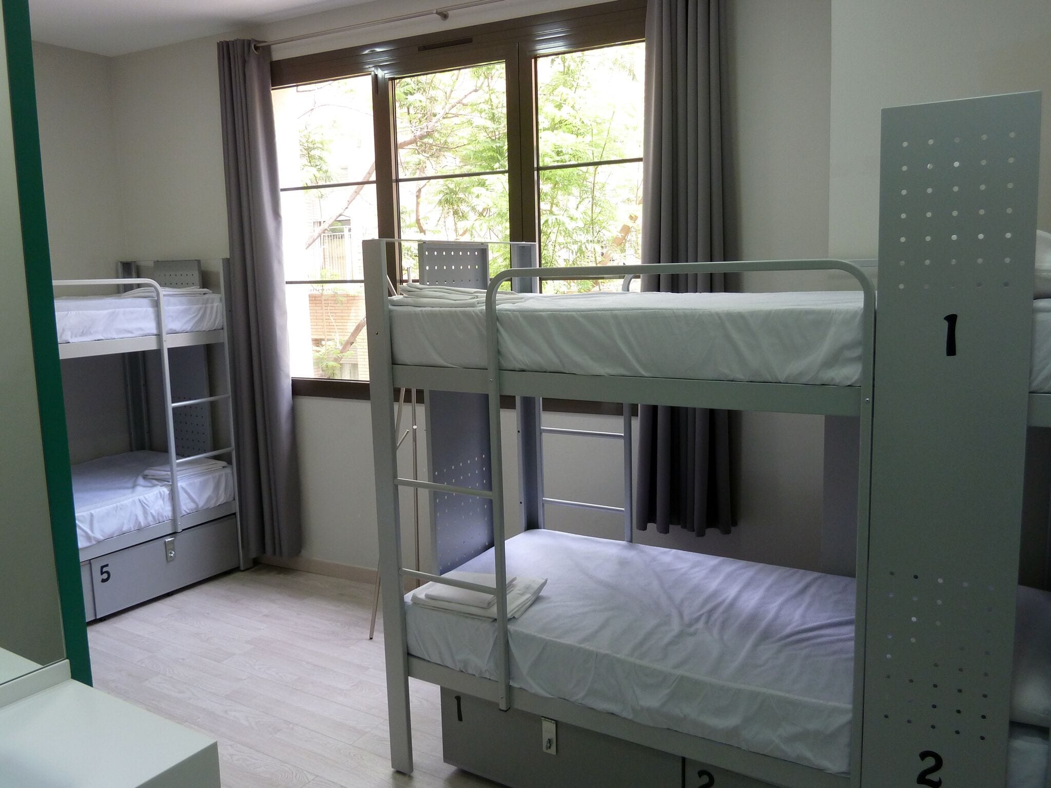 Een slaapzaal met stapelbedden, een raam met gordijnen en een groene muur met een nummer.