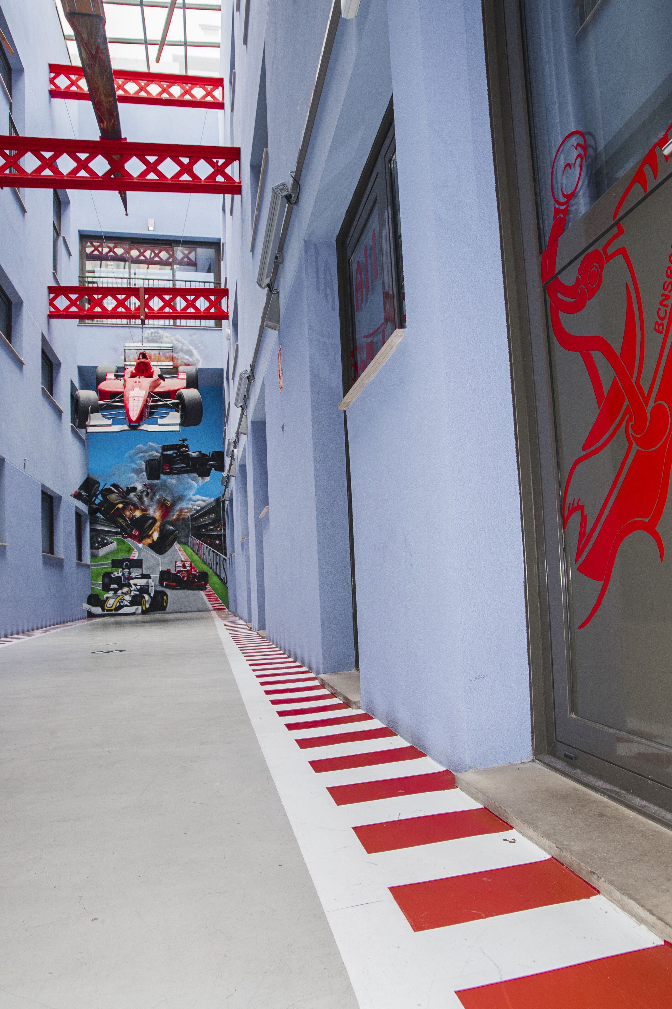 Un pasillo estrecho con suelo a rayas rojas y blancas, un mural de coches de carreras en la pared y el logotipo de un dragón rojo en la puerta.