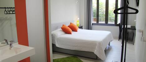 Quarto de hotel com uma cama, um tapete verde, uma pia branca e uma janela com cortinas.