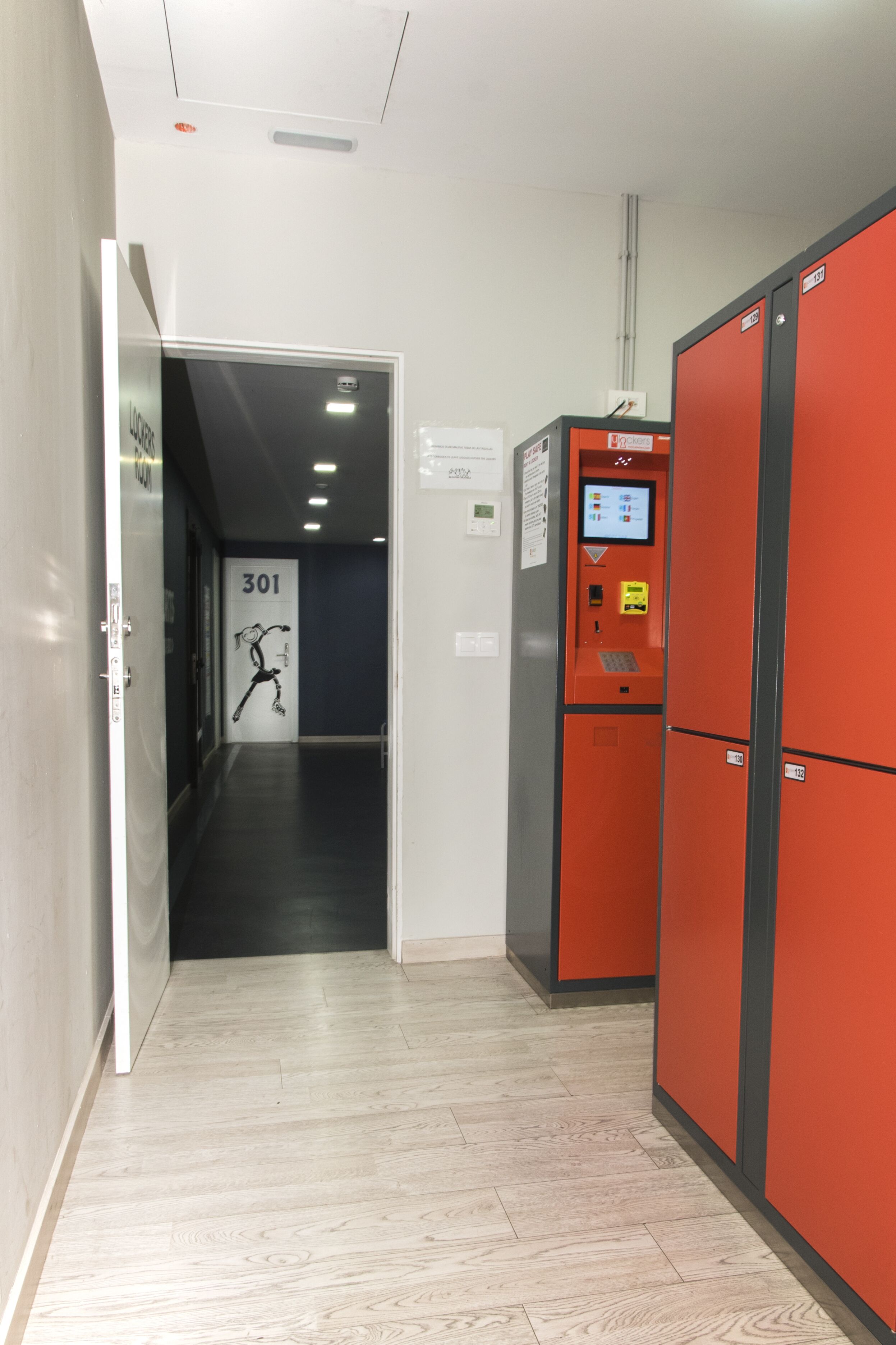 Un pasillo con una puerta identificada con el número 301, una máquina expendedora roja y una cámara de seguridad en la pared.