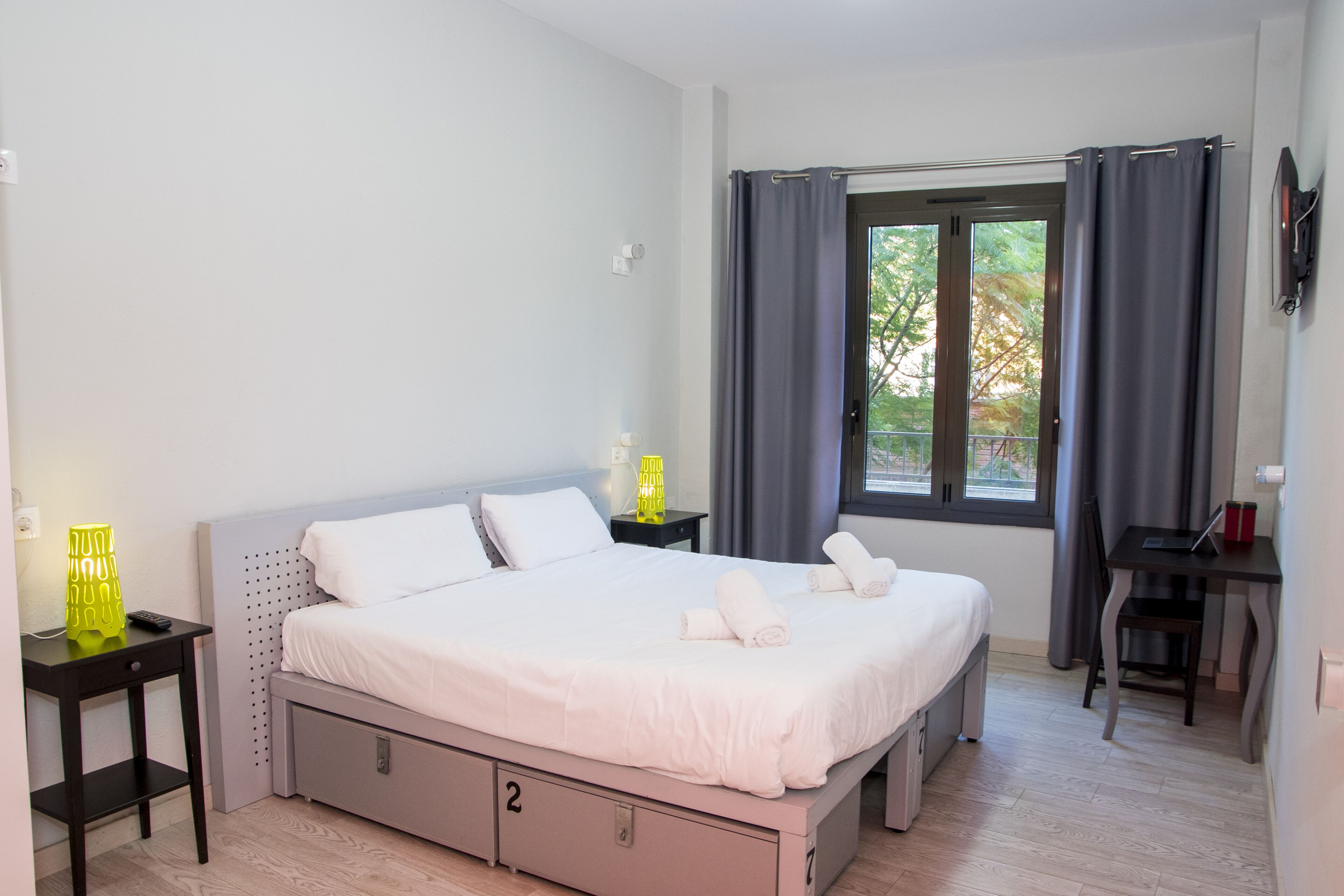 A bedroom with a bed, bedside tables, a desk, and a window with curtains.