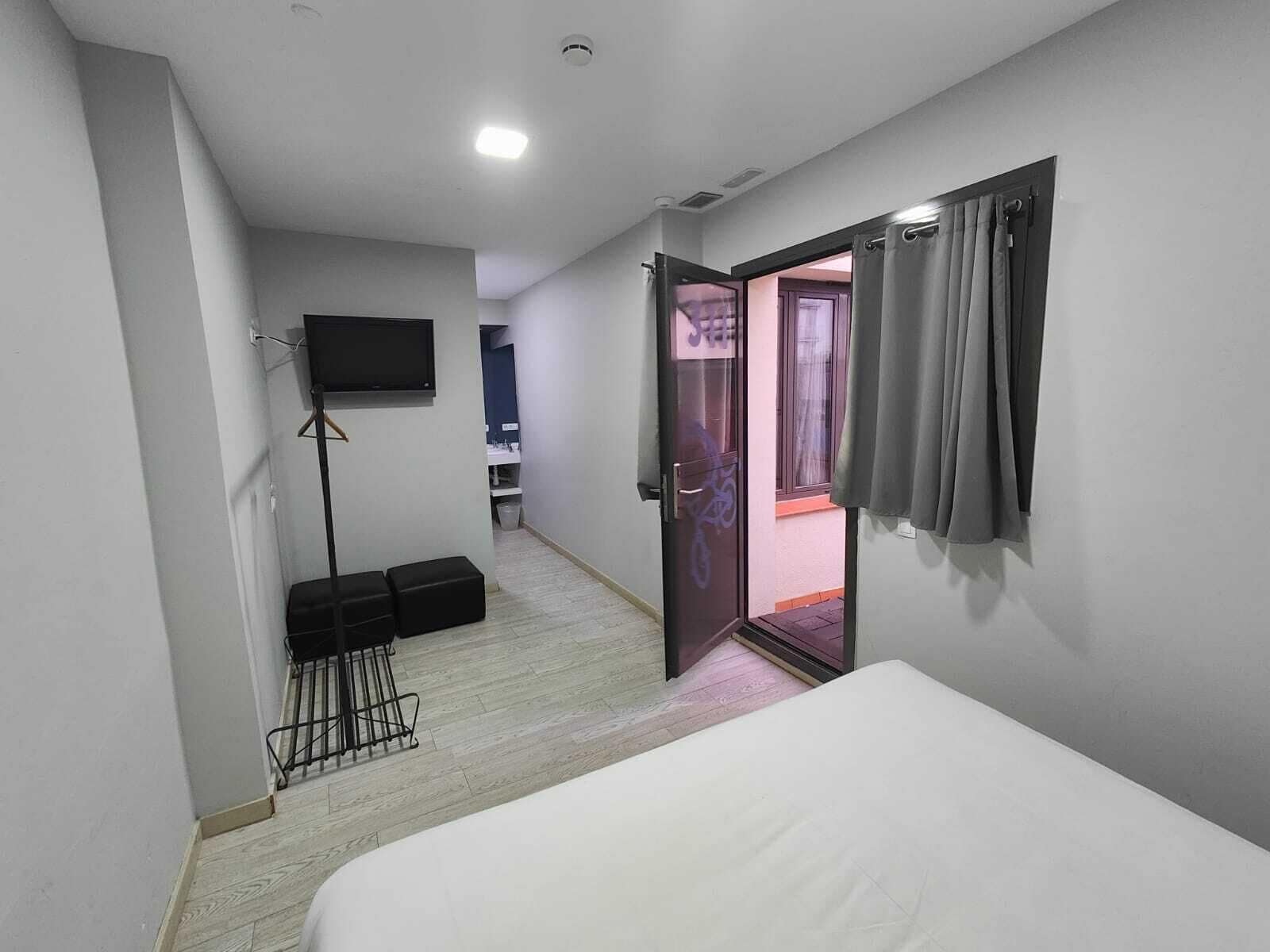 Een slaapkamer met een bed, een aan de muur bevestigde televisie, een deur naar een balkon en een zithoek met een kruk en een stoel.