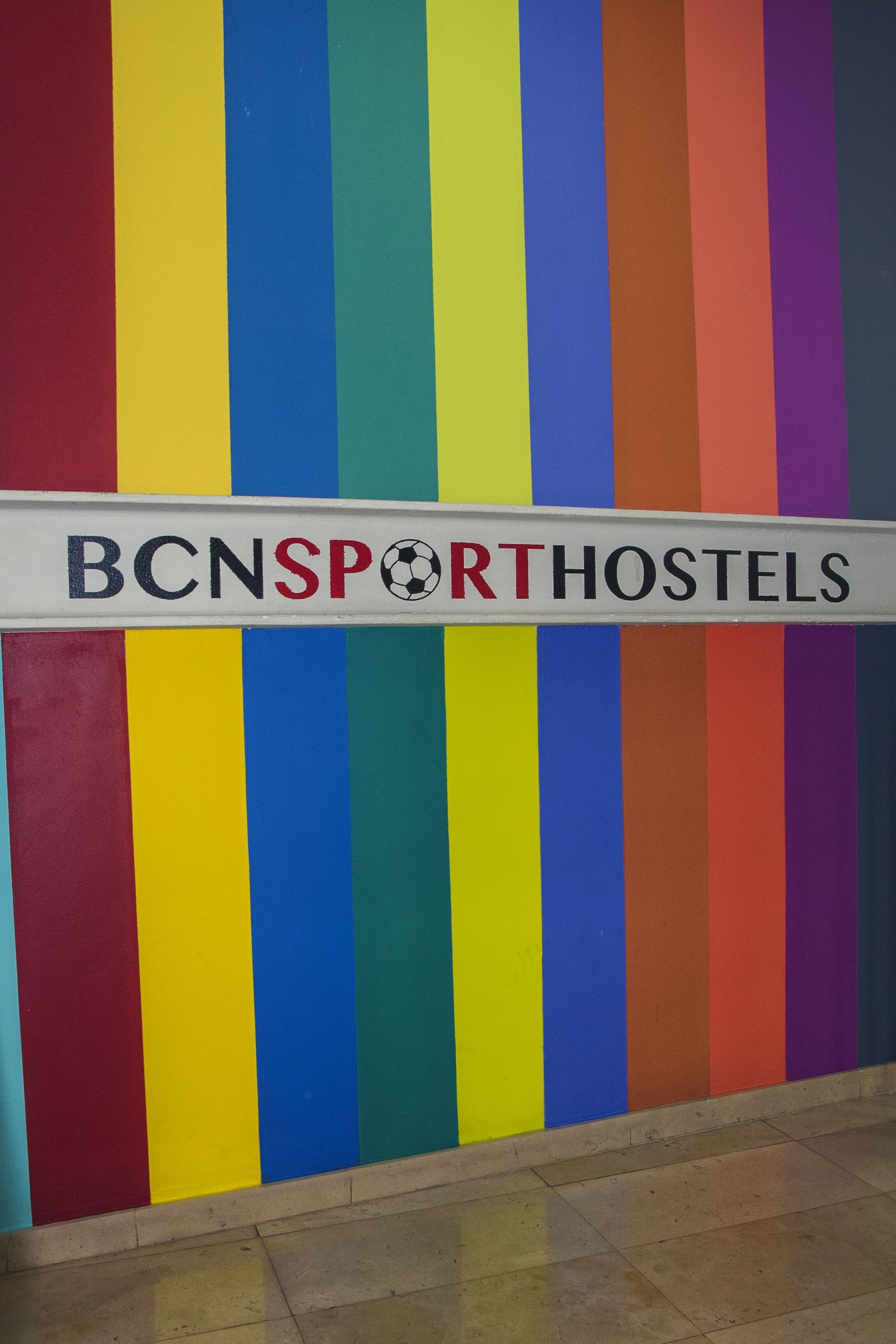 Una pared colorida con rayas verticales y un letrero que dice "BCNSPORTHOSTELS".