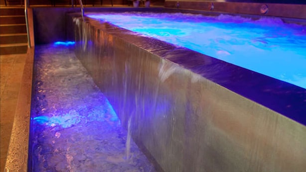 Une piscine éclairée de lumières bleues, une terrasse en bois et des chaises longues.