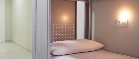 A single-bed room with a bunk bed structure, a wall-mounted light, and a door.